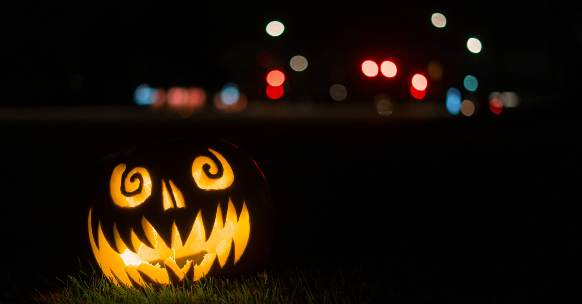 A jack-o-lantern sits lit up on the grass against a black sky